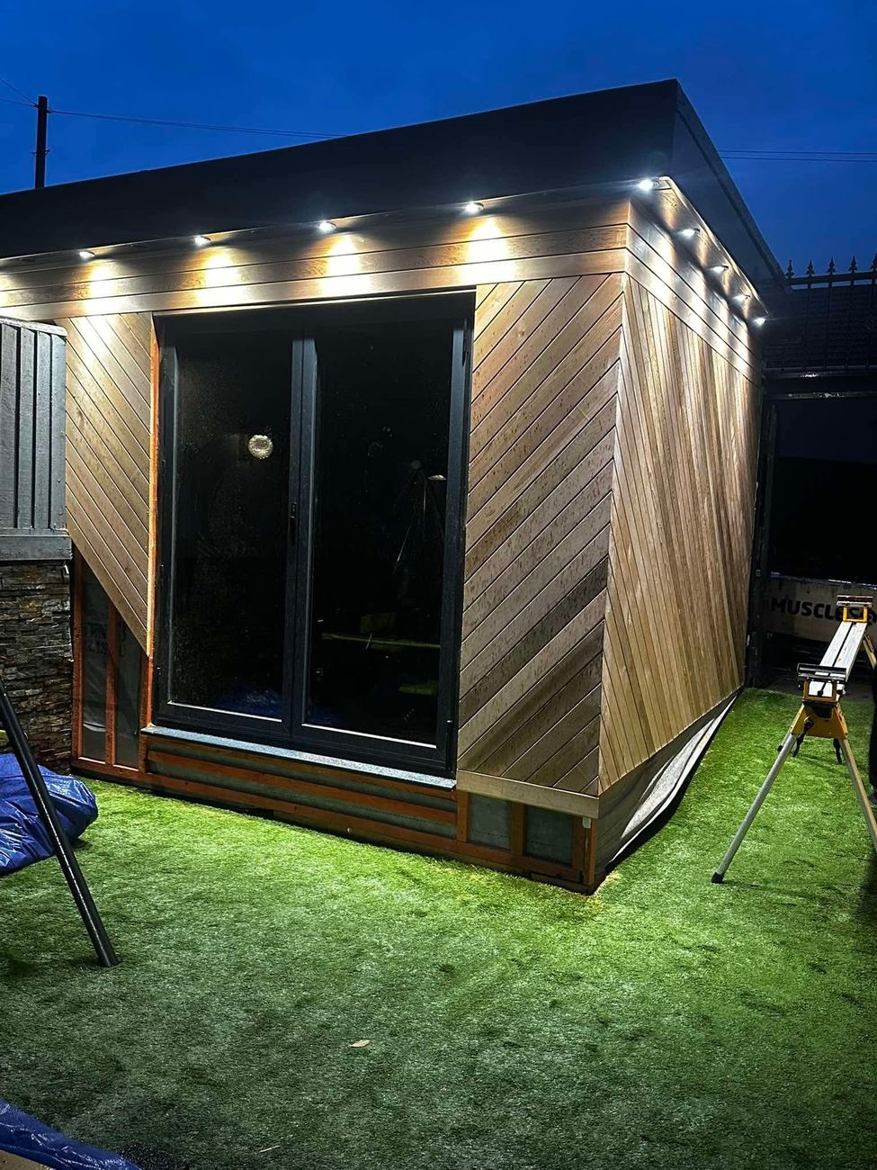 Cedar-clad garden room lit up at dusk with downlights in the roof overhang