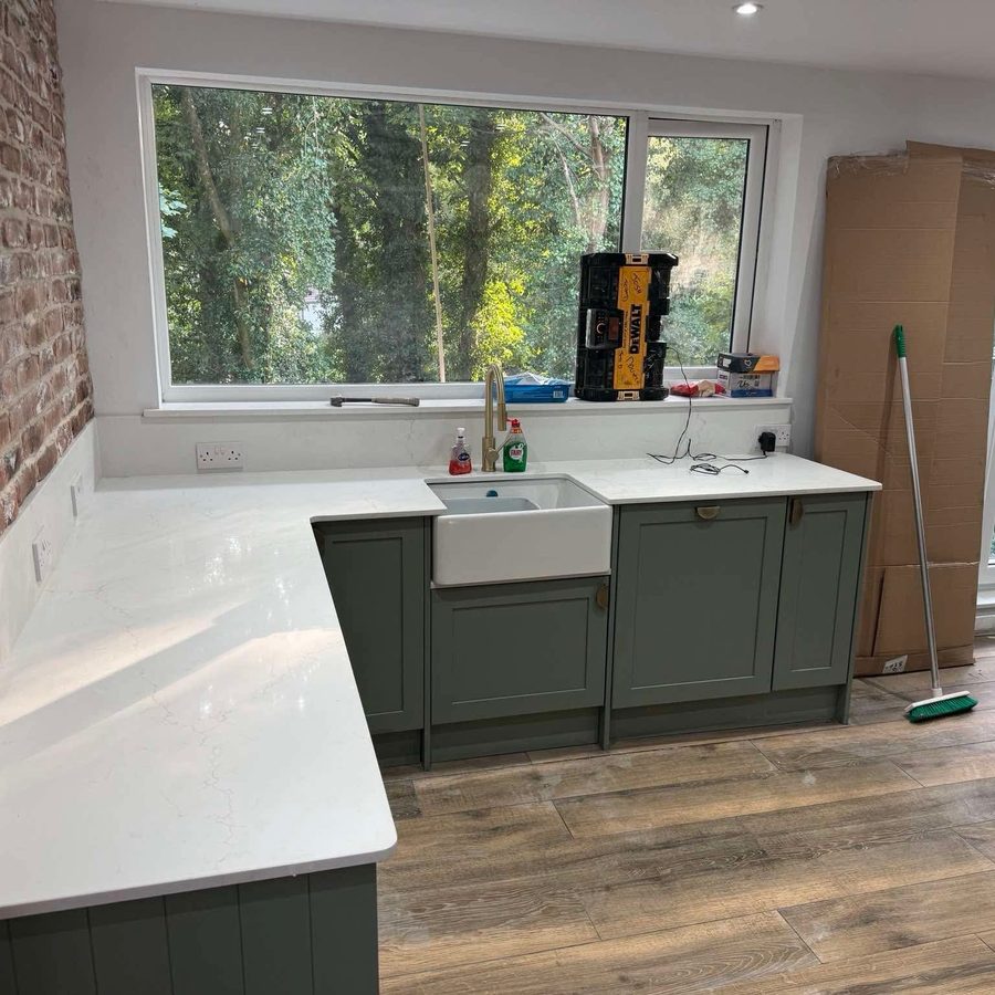 Green shaker kitchen with quartz worktops, Belfast sink and brick wall